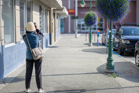 Woman taking photos using a smartphone. Beautiful flower baskets hanging on the lamp posts. Downtown Anchorage. Alaska.の写真素材