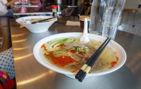 Chinese chilly noodle soup on the table. Unrecognizable people enjoying lunch in a restaurant.