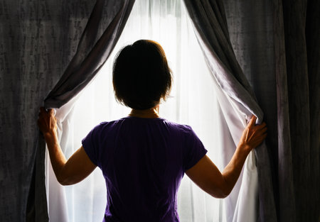Woman opening the curtains and letting morning sunlight in. Bright sunny day outside.の写真素材