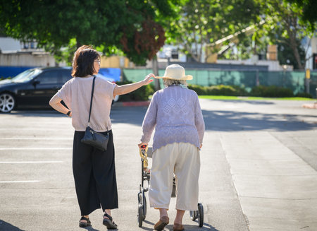 Senior woman walking using a mobility walker in the carpark. Adult daughter adjusting elderly motherâs hat. California.の写真素材
