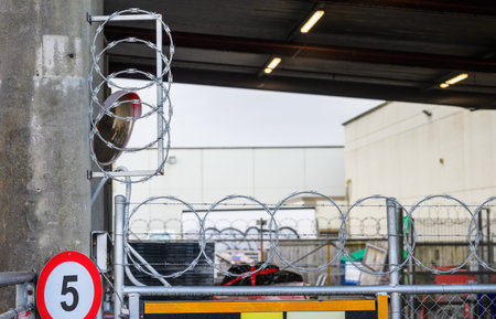 Razor and barbed wire topping a security fence. 5 kmh speed limit sign on the post.