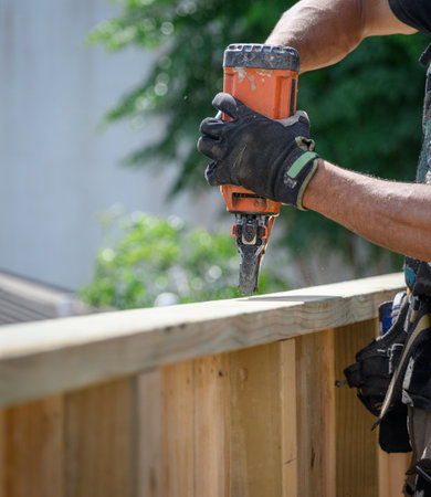 Hands of a professionally equipped builder working on fence using a nail gun construction tool.の写真素材
