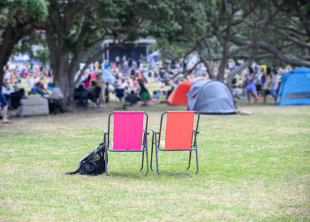 Two empty camping chairs, unrecognizable crowds listen to the music concert in the park. Auckland.の写真素材