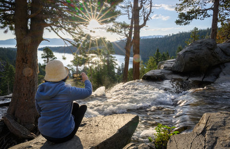 Woman taking photos of Lower Eagle Falls using smartphone at sunrise. Emerald Bay. South Lake Tahoe. California.の写真素材