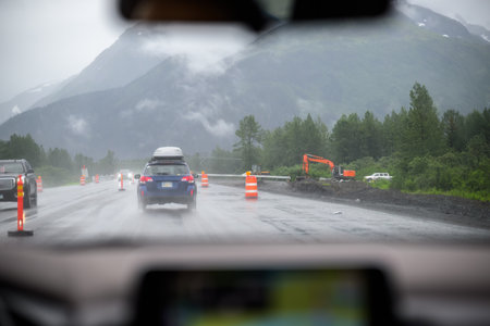 Cars travelling on Seward Hwy in the rain. Traffic cones and digger machines by the roadside. Alaska. USA.の写真素材
