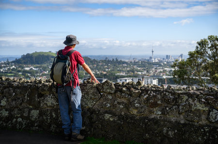 Man standing by stone wall on One Tree Hill, enjoying the views of Sky Tower and Auckland city.の写真素材