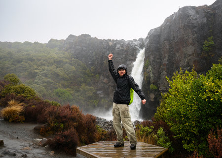 Tourist posing for fun photos at Taranaki Falls in the rain. Tongariro National Park. New Zealand.の写真素材