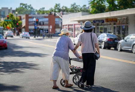Senior woman walking using a mobility walker, crossing the street with the help of adult daughter. California.の写真素材