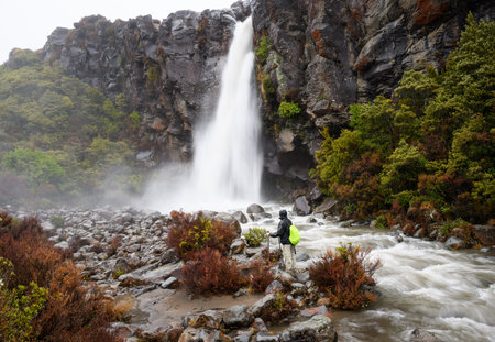 Man standing at the base of Taranaki Falls, enjoying the waterfalls in the rain. Taranaki Falls track. Tongariro National Park. New Zealand.の写真素材