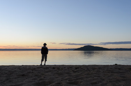 Man standing along on the beach at sunset. Mokoia Island in the distance. Lake Rotorua.の写真素材