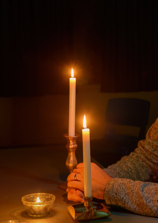 Crossed hands and lit candles in the dark. An empty chair in the background. Vertical format.の写真素材