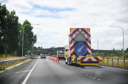 Roadwork arrow sign on back of the work truck. Orange traffic cones and unrecognizable cars driving on the road. Waikato. New Zealand.の写真素材