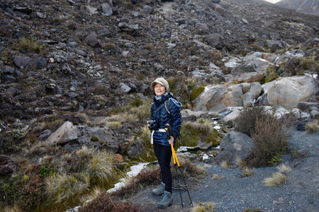 Woman holding a camera and hiking poles at Tongariro Alpine crossing. Tongariro National Park. New Zealand.の写真素材