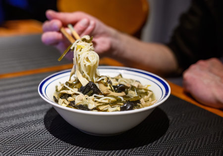 Hands of a man picking up noodles with chopsticks. Home-made Chinese northern noodles with gravy.