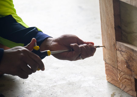 Hands of a worker using manual screwdriver on wooden box.の写真素材