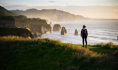 Woman standing on the top of the hill at sunset. Three Sisters rock formation at Tongaporutu. Taranaki.の写真素材