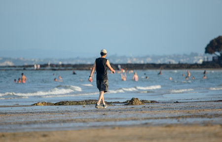 Man walking on the beach. Out-of-focus crowd playing in the water in summer, Auckland.の写真素材