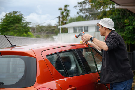 Man washing car on the driveway using a brush and water spray from a hose.の写真素材