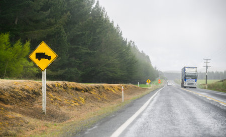 Truck Crossing sign on the roadside in the rain. Truck and cars travelling on the road. North Island. New Zealand.の写真素材