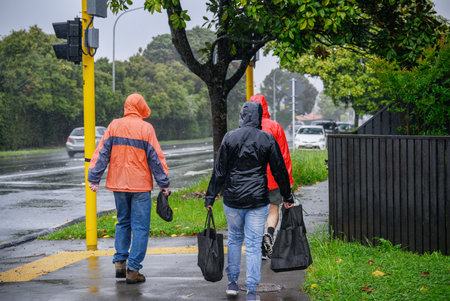 People carrying shopping bags and walking on the pedestrian footpath in the rain. Auckland.の写真素材