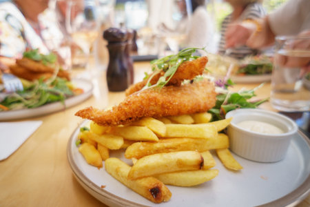 Fish and chips on a plate. Unrecognizable people dining in the restaurant. Auckland.の写真素材