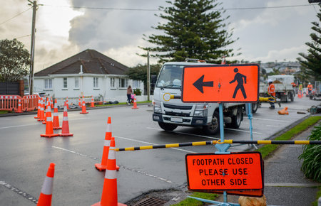 Footpath Closed road sign by the road. Unrecognizable workers on the road. Roadworks in Auckland.