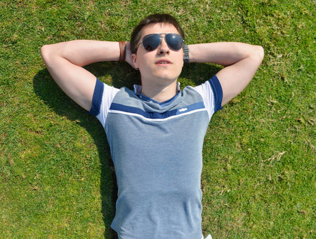 Young man in sunglasses lying on a green grass