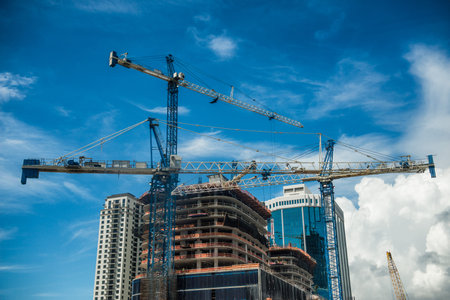 Cranes on modern skyscraper construction in city at sunny day with blue sky 