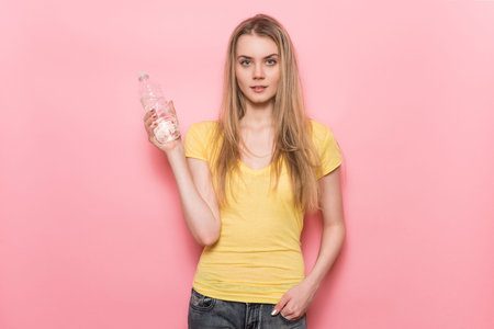 Beautiful young woman with perfect body holding plastic water bottle standing near the wall.の写真素材