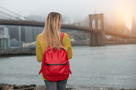 Young tourist woman traveling in New New York city with red backpack and looking to Brooklyn Bridge.の写真素材