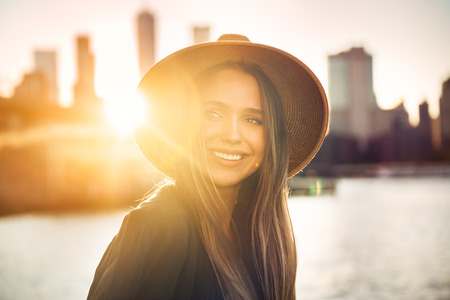 Close-up portrait of beautiful smiling woman looking to the side on the beach in city.の写真素材