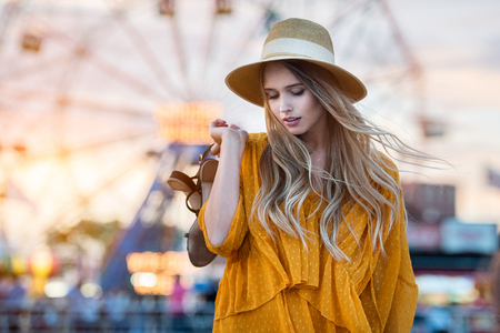 Bare feet woman walking on the beach holding sandals in hand at sunset time near amusement park rides.の写真素材