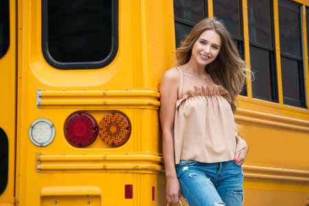 Beautiful high school student standing near yellow school bus