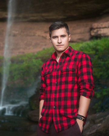 Handsome tourist man traveling and wearing plaid red shirt looking at camera on nature waterfall background.の写真素材