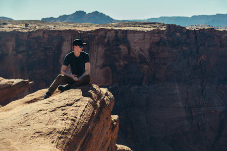Tourist man sitting on the mountain cliff edge rock and enjoing the view after hiking at hot summer day ar Grand Canyonの写真素材