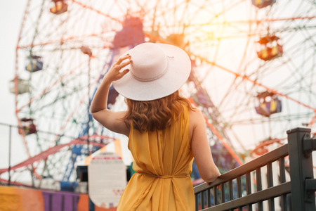 Beautiful elegant woman looking at her kids on ferris wheel in amusement park wearing hat and summer dressの写真素材