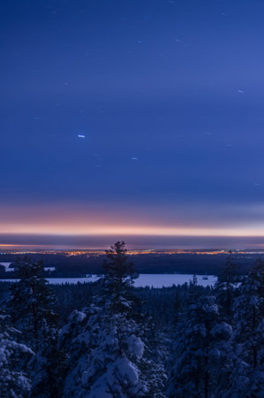 View of a frozen lake in middle of forests with city lights on the horizon in Finland