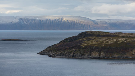 Mountains by a fjord with some snow and a hill in front in northern Norwayの写真素材