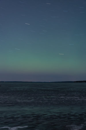 Green aurora borealis hue and rotating stars over a frozen lake in Tampere, Finlandの写真素材