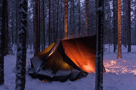 A traditional shelter in a snowy forest in Patvinsuo National Park in Eastern Finland with the warm light of campfire insideの写真素材