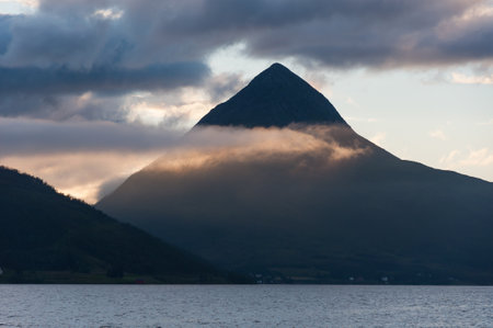 Pyramid shaped mountain in northern Norway with glowing clouds passing in frontの写真素材