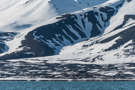 Snow covered and partly rocky mountainsides by an arctic fjord in Svalbardの写真素材