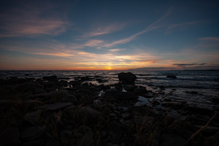 The rocky shores of the Bothnian sea with the sunset coloured horizon in the background in Pori,...