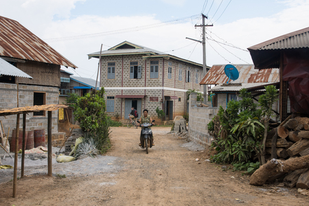 man riding motorcylce in local dirt road with colorful houses near inle lake in myanmarのeditorial素材