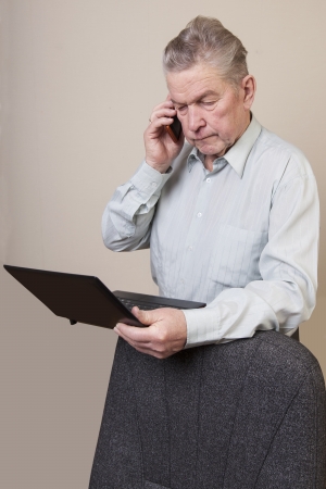 Senior man using laptop and phone.の写真素材
