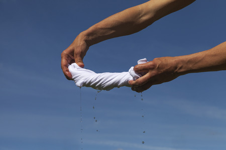 Hands squeeze wet fabric against blue sky.の写真素材
