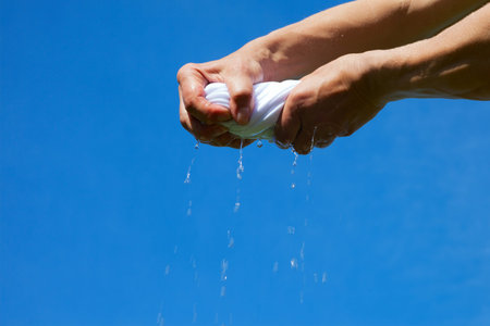 Hands squeeze wet fabric against blue sky.の写真素材