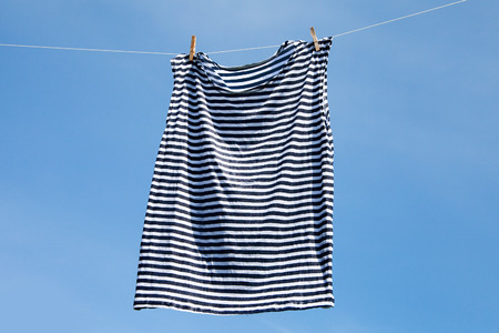 Wet striped shirt on clothesline against blue sky.の写真素材