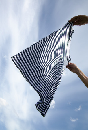 Wet striped shirt in hands against blue sky.の写真素材