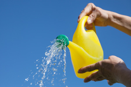 Pouring water and watering can against blue sky.の写真素材